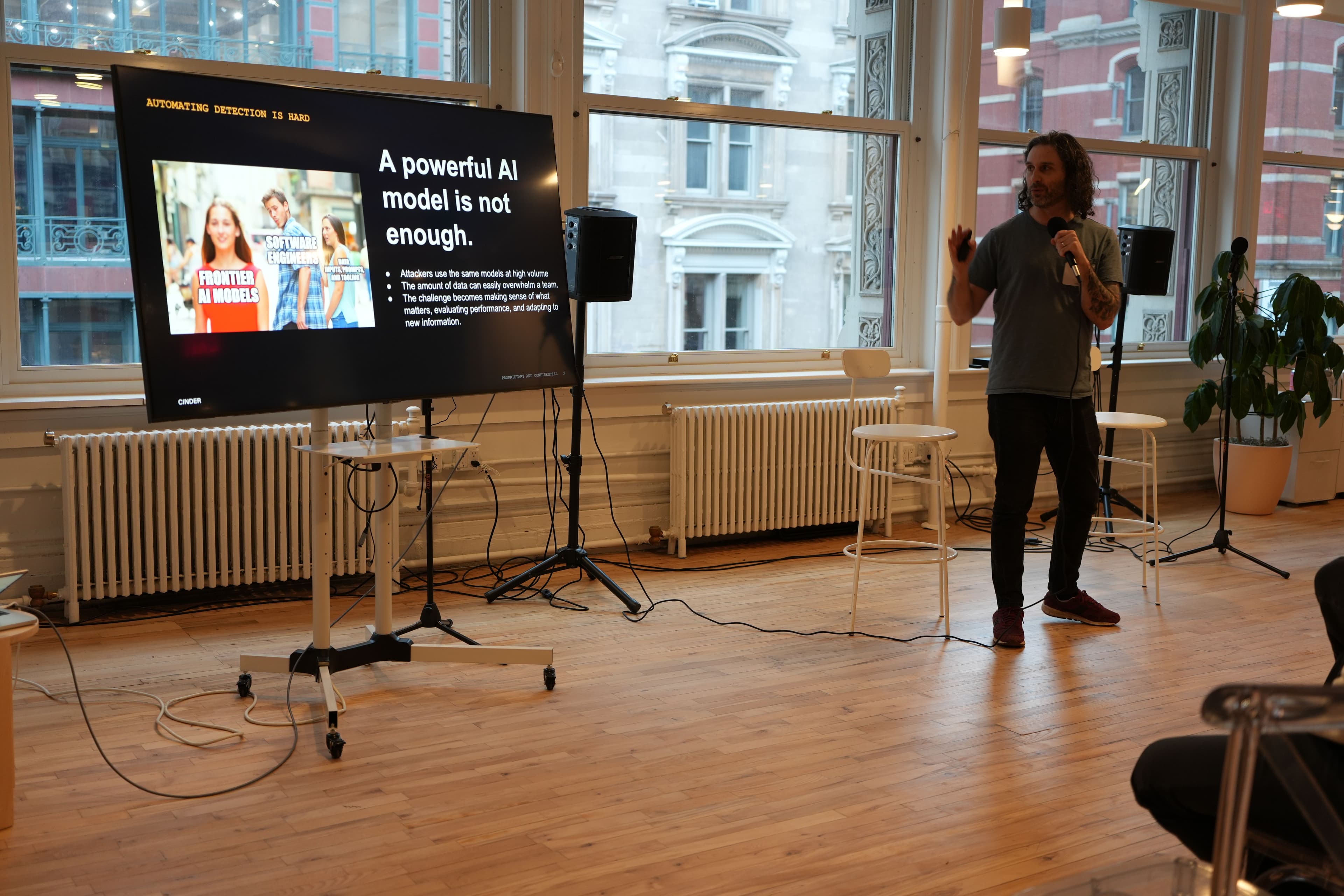 Chris Grigg speaking at Cinder's New York City headquarters beside a presentation slide about automating detection